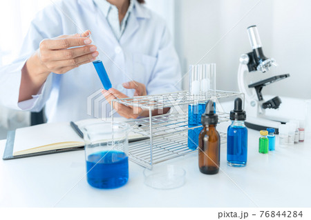 Scientist woman holding test tube in his hands and checking blue liquid from test tube while working 76844284