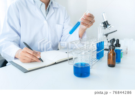 Scientist woman holding test tube in her hands and writing down result report on notebook while working 76844286