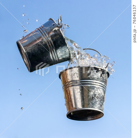 A pouring water from falling bucket to bucket, on a background of blue sky. A pouring water from falling bucket to bucket, on a background of blue sky. 76846137