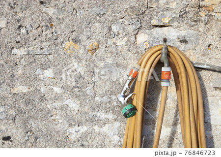 Coiled garden hose hanging on faucet against stone wall 76846723