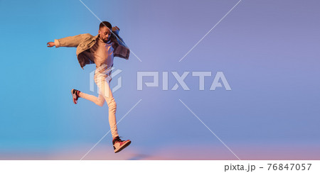 Young stylish man in modern street style outfit isolated on gradient background in neon light. African-american fashionable model in look book, musician performing. 76847057