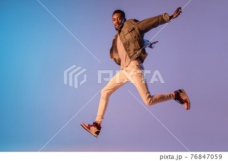 Young stylish man in modern street style outfit isolated on gradient background in neon light. African-american fashionable model in look book, musician performing. 76847059