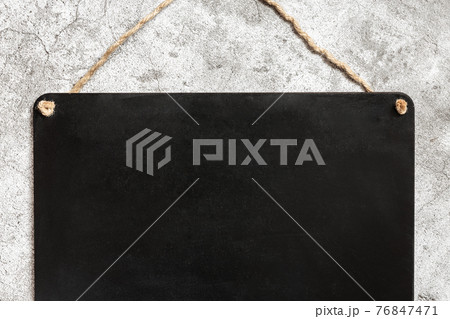 A fragment of a slate chalk black board on a rope, a plate hangs on a concrete wall a blank for writing text 76847471