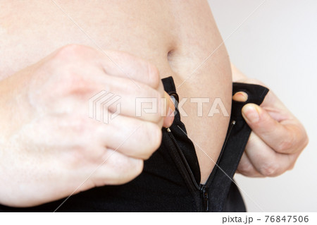 A fat man tries to fasten his pants on his big belly. A fat man tries to fasten his pants on his big belly. 76847506