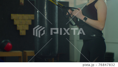 Blonde woman in sportswear doing exercise with TRX system at gym. Cross training. Modern fitness. Blonde woman in sportswear doing exercise with TRX system at gym. Cross training. Modern fitness. 76847832