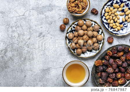 Popular food during Iftar - macadamia nuts, pistachios, walnuts, dry dates. Karan, rosary, teapot, bowl with black tea on concrete background Top view Flat lay Muslim holiday of holy month of Ramadan 76847987