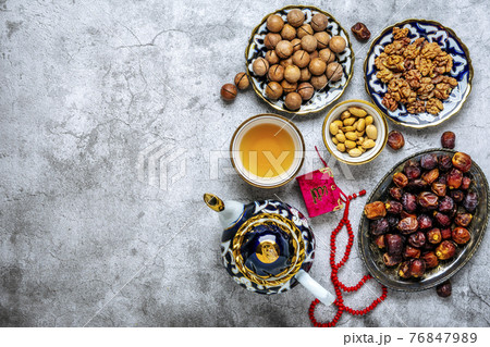 Popular food during Iftar - macadamia nuts, pistachios, walnuts, dry dates. Karan, rosary, teapot, bowl with black tea on concrete background Top view Flat lay Muslim holiday of holy month of Ramadan 76847989