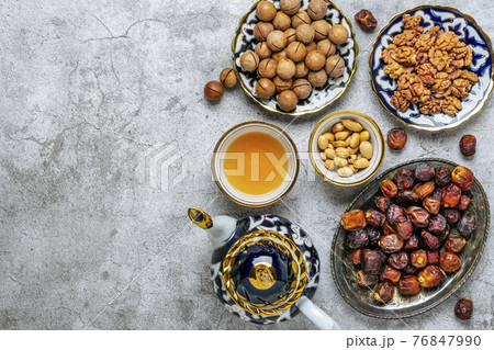 Popular food during Iftar - macadamia nuts, pistachios, walnuts, dry dates. Karan, rosary, teapot, bowl with black tea on concrete background Top view Flat lay Muslim holiday of holy month of Ramadan 76847990