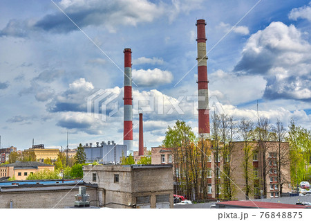 Tall factory chimneys against backdrop of a cloudy sky and residential buildings 76848875