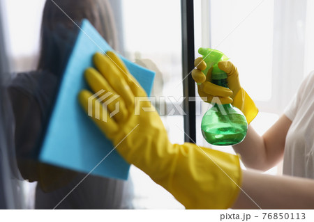Female hands in yellow gloves wash windows with rag and cleaning agent Female hands in yellow gloves wash windows with rag and cleaning agent 76850113