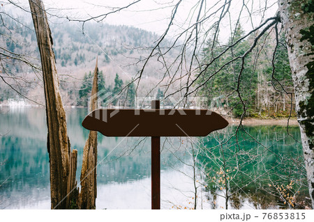 Unmarked road sign stands near a lake in the forest against a background of mountains Unmarked road sign stands near a lake in the forest against a background of mountains 76853815