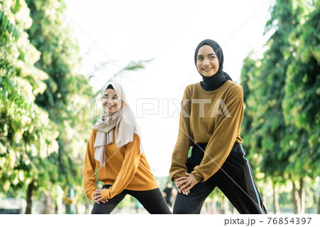 beautiful two Muslim girls in headscarves do lunges movement before outdoor sports 76854397