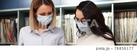 Two women wearing protective medical masks selecting fabric from catalog Two women wearing protective medical masks selecting fabric from catalog 76856177