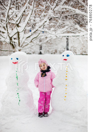The child plays with snow in the winter. A little girl in a bright jacket and knitted hat, catches snowflakes in a winter park for Christmas. 76860278