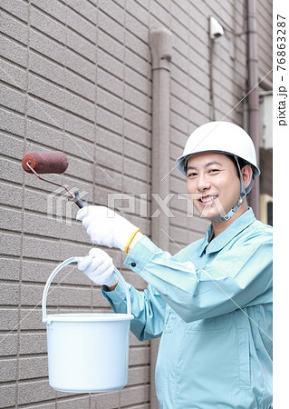 一軒家の外壁に塗装をする作業員の男性 76863287
