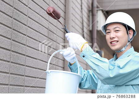 一軒家の外壁に塗装をする作業員の男性 76863288