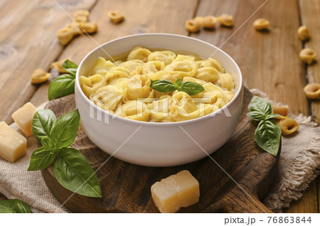 Tortellini mignon on a wooden board with basil and parmesan. Specialties of the cuisine from Bologna 76863844
