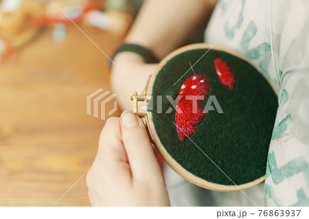 Girl is embroidering mushroom cap on green cloth. 76863937