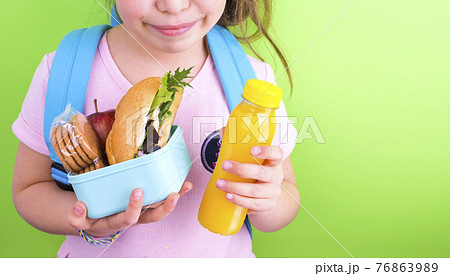 Young schoolgirl with lunch box on a green background. Little girl with a school backpack and a set 76863989