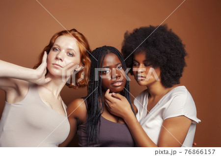 young pretty caucasian, afro, scandinavian woman posing cheerful together on brown background, lifestyle diverse nationality people concept 76866157