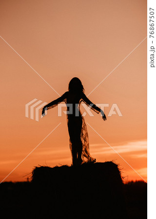 Silhouette of a sexy girl in a transparent dress in summer at sunset in a field 76867507