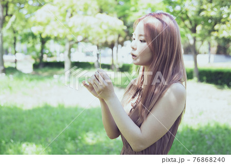 たんぽぽの綿毛を吹く美しい女性のポートレートの写真素材 [76868240 