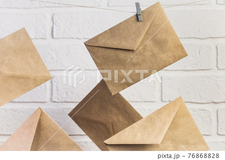 Concept postal communication background, several new paper brown craft letter envelopes hang on clothespins on a rope against a white wall background 76868828