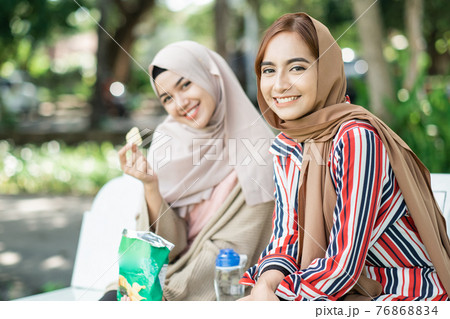muslim young woman with friend enjoy their snack while relaxing in the park 76868834