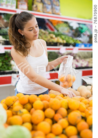 Portrait of young woman buying tangerines at grocery store Portrait of young woman buying tangerines at grocery store 76870900