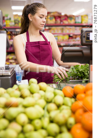 Young saleswoman weighs greens on a scale 76871279