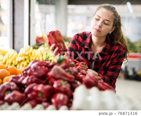 Portrait of a young female in a store, choosing a bell pepper 76871316