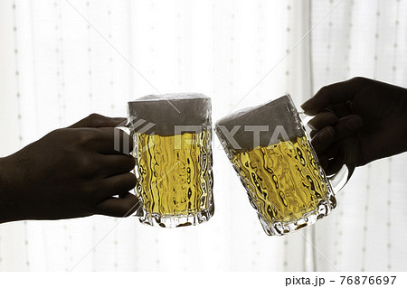 カーテンレースの前で、ビールで乾杯する男女の手 76876697