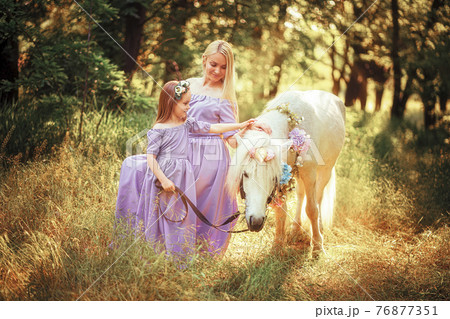 Mother and daughter in similar lavender dresses are petting a un Mother and daughter in similar lavender dresses are petting a un 76877351