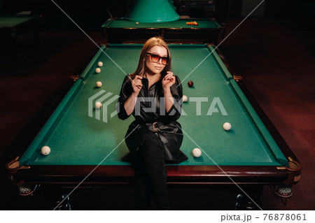A girl with glasses sits on a pool table in a club.Russian billiards 76878061
