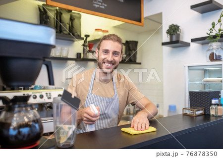 Happy man with napkin and disinfectant behind bar Happy man with napkin and disinfectant behind bar 76878350