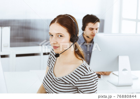 Casual dressed young woman using headset and computer while talking with customers online. Group of operators at work. Call center, business concept 76880844