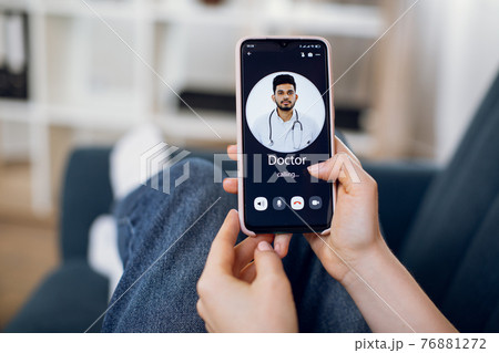 Close-up back view of female patient hands, using smart phone and calling to her doctor, young Indian man. App for remote medical service Close-up back view of female patient hands, using smart phone and calling to her doctor, young Indian man. App for remote medical service 76881272