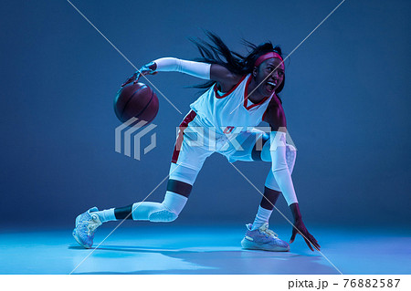 Beautiful african-american female basketball player in motion and action in neon light on blue background. Concept of healthy lifestyle, professional sport, hobby. 76882587