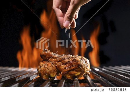 Hand sprinkling salt and spices on grilled chicken leg on the flaming grill Hand sprinkling salt and spices on grilled chicken leg on the flaming grill 76882613