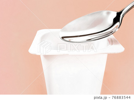 Yogurt cup and silver spoon on beige background, white plastic container with yoghurt cream, fresh dairy product for healthy diet and nutrition balance 76883544