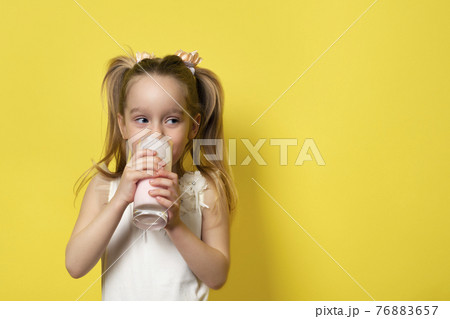Little girl drinks yogurt from a glass isolated on yellow background. Healthy eating concept. Banner with copy space. 76883657