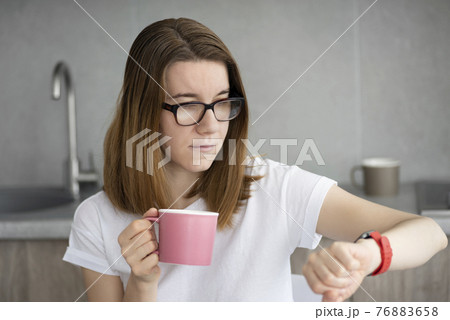 young woman drinking coffee and looking at wristwatch in modern kitchen. Time management concept young woman drinking coffee and looking at wristwatch in modern kitchen. Time management concept 76883658