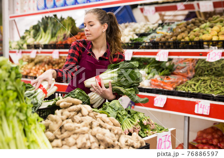Portrait of a young saleswoman laying out bundles of chinese cabbage on the counter Portrait of a young saleswoman laying out bundles of chinese cabbage on the counter 76886597