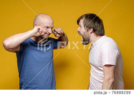 Two men, one in a rage screams loudly at the other who covered his ears with his fingers and looks 76888299