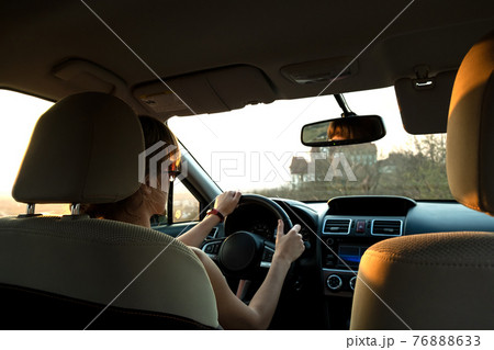 Close up view of a woman driver holding steering wheel driving a car at sunset. 76888633