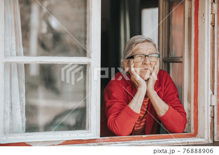 Portrait of lovely senior woman or grandmother watching out from the window and smiling 76888906