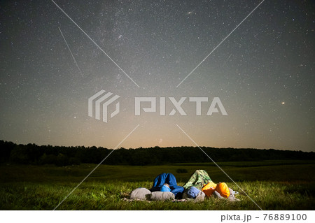 People resting in night field observing dark sky with many bright stars. People resting in night field observing dark sky with many bright stars. 76889100