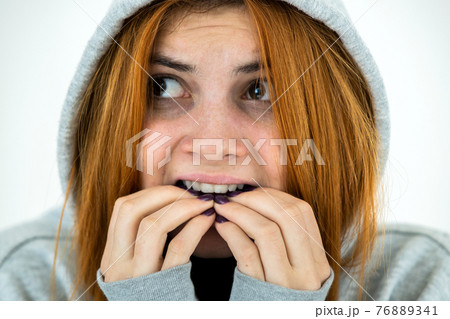 Close up portrait of scared young redhead woman wearing warm hoodie pullover. 76889341