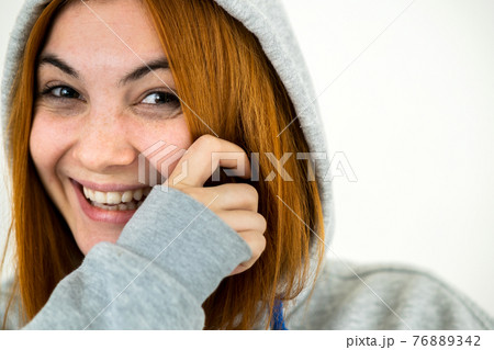 Close up portrait of happy smiling young redhead woman wearing warm hoodie pullover. 76889342
