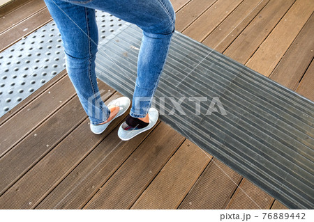 Female legs in denim jeans pants and light summer sneakers standing on wooden floow. Female legs in denim jeans pants and light summer sneakers standing on wooden floow. 76889442